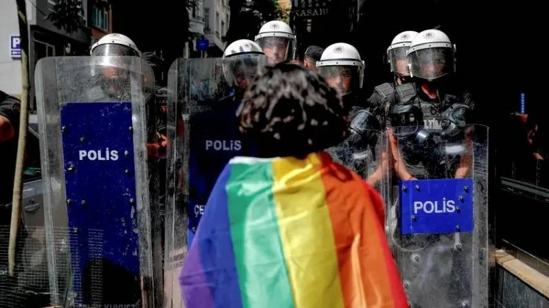 Une personne portant un drapeau arc-en-ciel sur les épaules fait face à des policiers à Istanbul